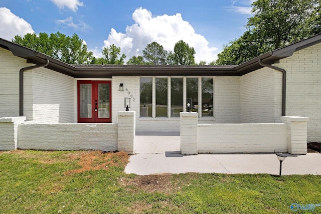 entrance to property featuring french doors, fence, a yard, and brick siding