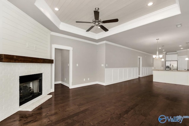 unfurnished living room with a fireplace, ceiling fan with notable chandelier, dark hardwood / wood-style floors, and a tray ceiling