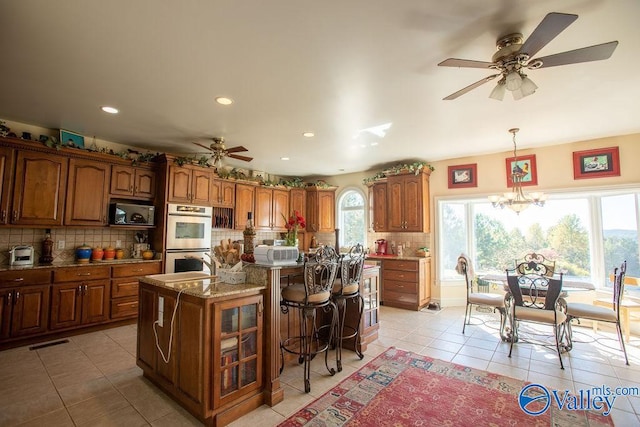 kitchen with a center island, ceiling fan with notable chandelier, tasteful backsplash, and double oven