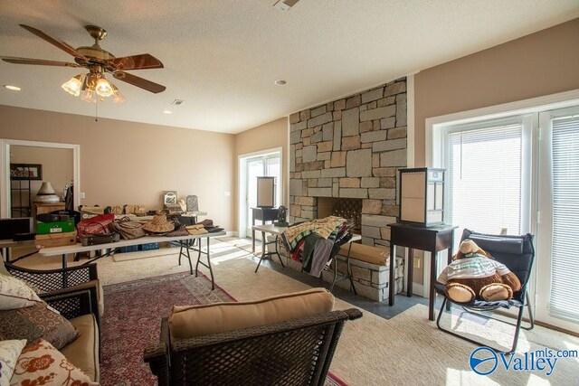 living room with a stone fireplace, light carpet, ceiling fan, and a textured ceiling