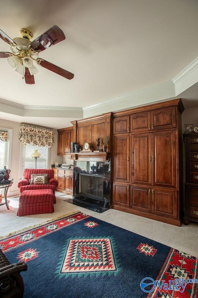 living room featuring ornamental molding, carpet flooring, ceiling fan, and a tray ceiling