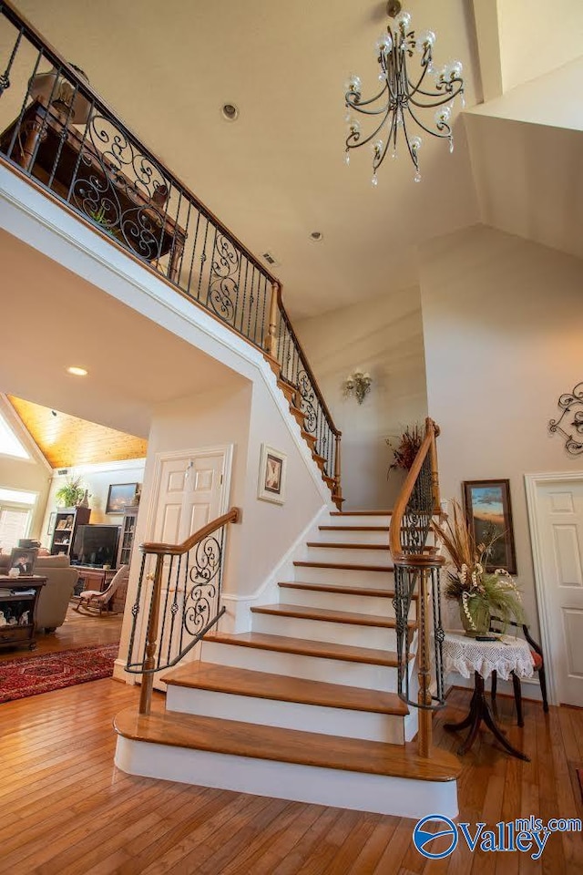 stairway featuring a notable chandelier, hardwood / wood-style floors, and high vaulted ceiling