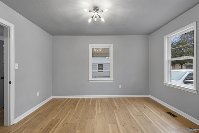 empty room with an inviting chandelier, a wealth of natural light, and light hardwood / wood-style flooring