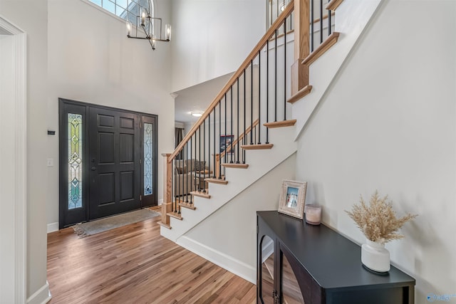 foyer entrance with a towering ceiling, wood finished floors, a chandelier, baseboards, and stairs