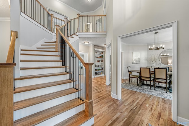 staircase with crown molding, a high ceiling, wood finished floors, baseboards, and an inviting chandelier