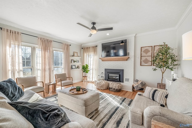 living area with crown molding, a brick fireplace, ceiling fan, wood finished floors, and baseboards