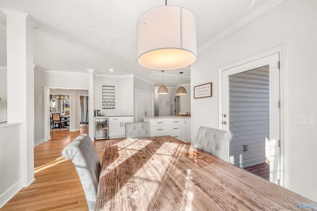 dining area with wine cooler, a dry bar, light wood finished floors, ornamental molding, and baseboards