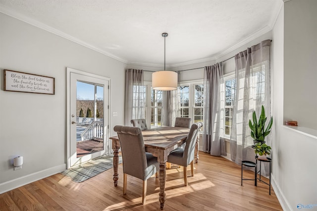 dining space with a textured ceiling, baseboards, light wood-style flooring, and crown molding