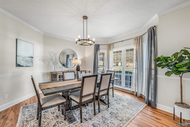 dining area featuring light wood-style floors, crown molding, a textured ceiling, and an inviting chandelier