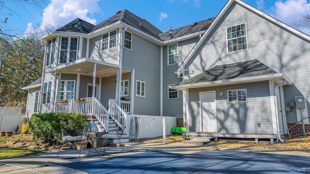 view of front of house with covered porch, a shingled roof, a patio area, and fence