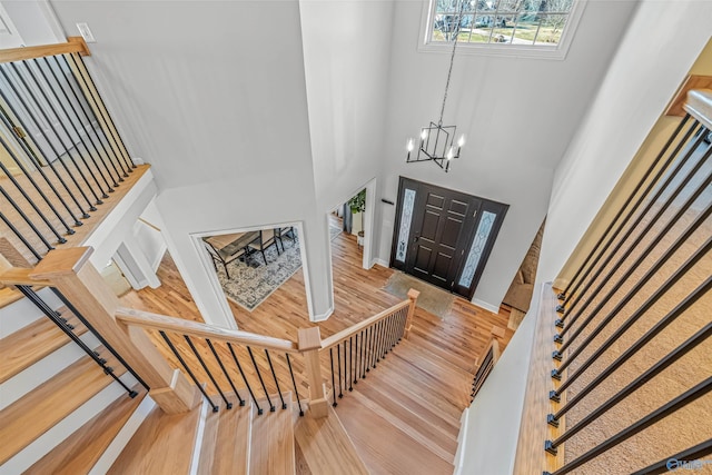 entryway with a towering ceiling, a notable chandelier, stairs, and wood finished floors