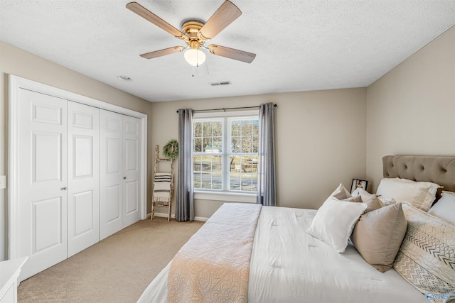 carpeted bedroom featuring a textured ceiling, a closet, visible vents, and a ceiling fan