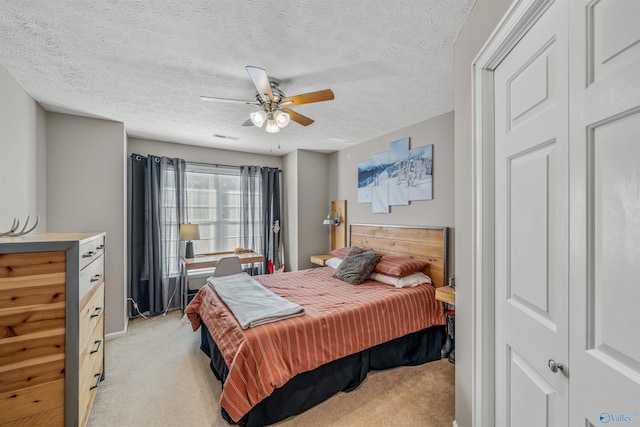 bedroom featuring light carpet, a textured ceiling, visible vents, and a ceiling fan