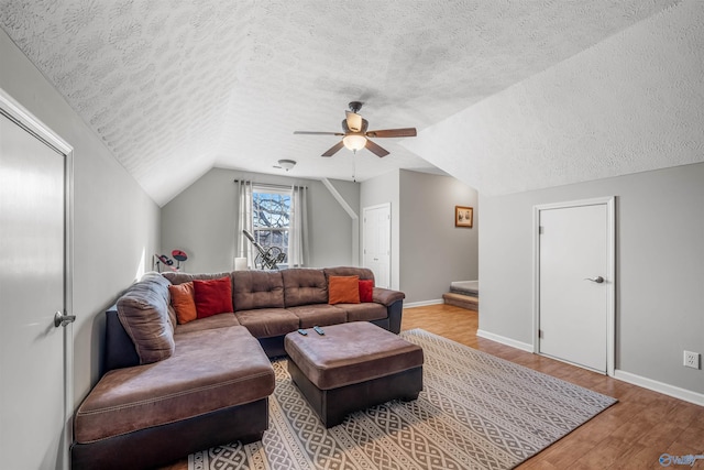 living area with light wood-style flooring, a ceiling fan, vaulted ceiling, a textured ceiling, and baseboards