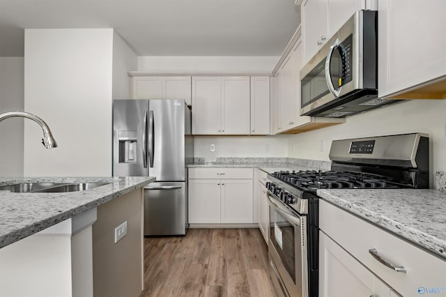 kitchen featuring sink, light stone counters, light wood-type flooring, stainless steel appliances, and white cabinets