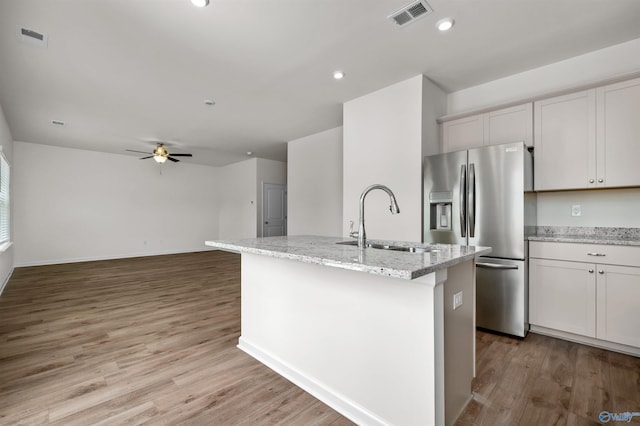 kitchen featuring stainless steel refrigerator with ice dispenser, sink, white cabinetry, an island with sink, and light stone countertops