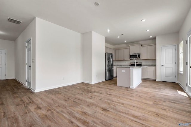 kitchen with light stone counters, appliances with stainless steel finishes, light hardwood / wood-style floors, and an island with sink