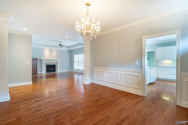 unfurnished living room featuring crown molding, decorative columns, ceiling fan with notable chandelier, a fireplace, and wood finished floors