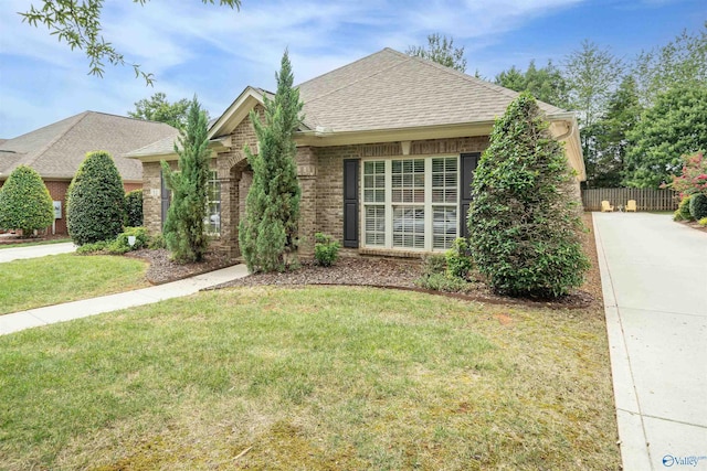 view of front of home with brick siding, a shingled roof, a front lawn, and fence
