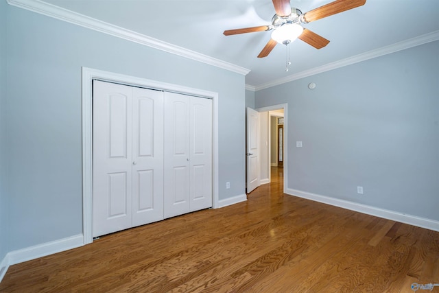 unfurnished bedroom with wood finished floors, baseboards, ceiling fan, a closet, and crown molding