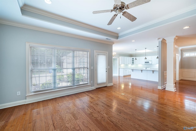 unfurnished living room with a raised ceiling, decorative columns, and wood finished floors