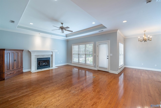 unfurnished living room with wood finished floors, baseboards, a tray ceiling, a tiled fireplace, and ceiling fan with notable chandelier