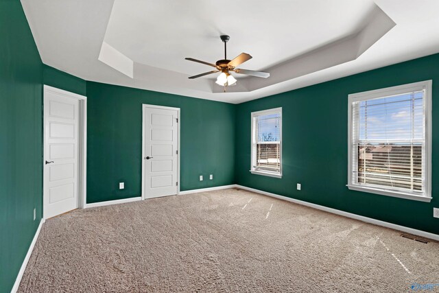 carpeted empty room featuring a tray ceiling, visible vents, ceiling fan, and baseboards