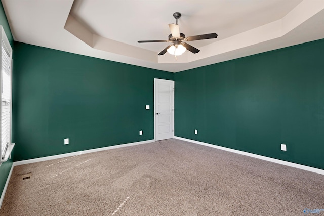 carpeted empty room with baseboards, a raised ceiling, and a ceiling fan