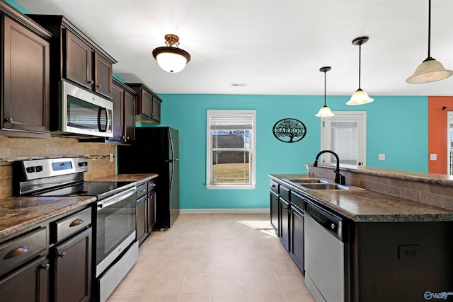 kitchen featuring dark brown cabinetry, a sink, appliances with stainless steel finishes, decorative backsplash, and dark countertops