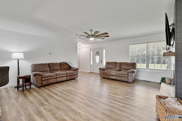 living room featuring a ceiling fan, visible vents, light wood finished floors, and baseboards