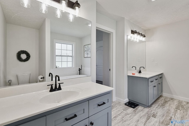 bathroom featuring hardwood / wood-style floors, a tub to relax in, vanity, a textured ceiling, and toilet