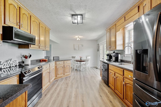 kitchen featuring dark countertops, light wood-type flooring, appliances with stainless steel finishes, a textured ceiling, and a sink