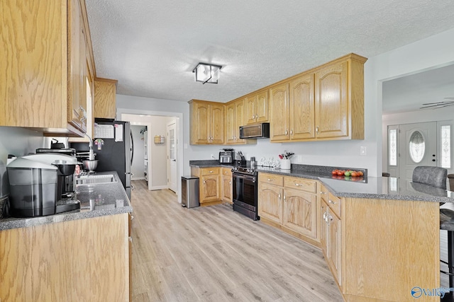 kitchen featuring electric range, light wood-style flooring, a kitchen breakfast bar, and a textured ceiling