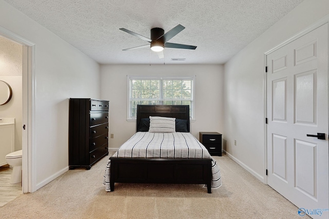 carpeted bedroom featuring visible vents, baseboards, ensuite bathroom, a textured ceiling, and a ceiling fan