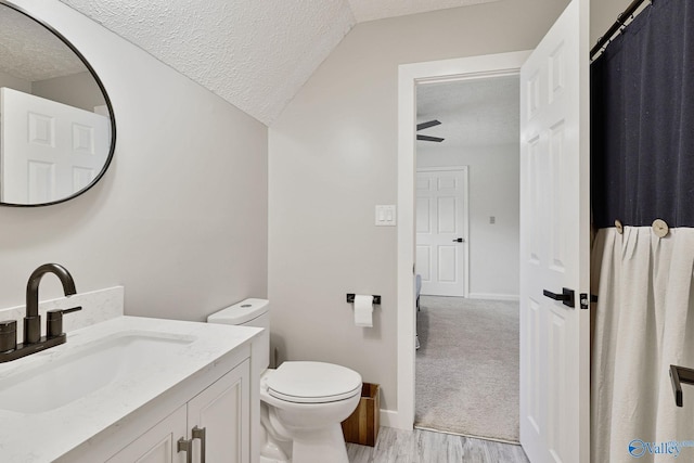 full bathroom with a textured ceiling, vaulted ceiling, vanity, and toilet