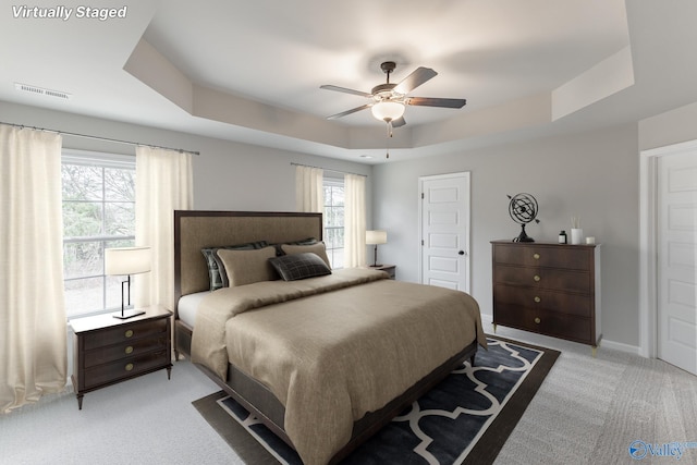 carpeted bedroom featuring multiple windows, a raised ceiling, and ceiling fan