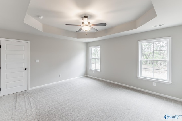 carpeted spare room with ceiling fan and a tray ceiling