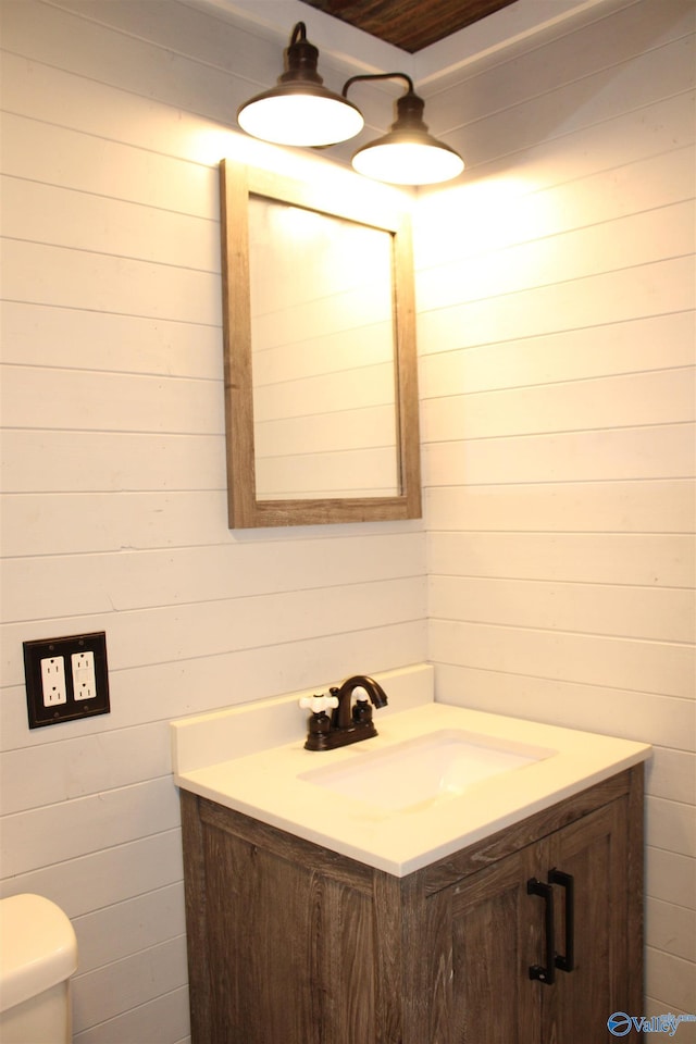 bathroom featuring toilet, wood walls, and vanity
