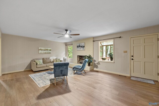 living room featuring light wood-style floors, a brick fireplace, baseboards, and ceiling fan