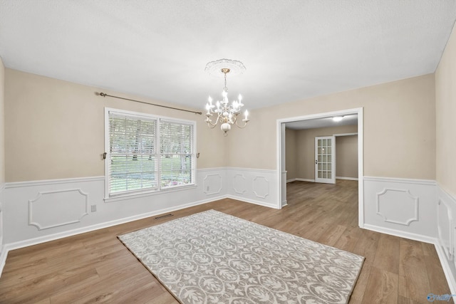 unfurnished dining area with wainscoting, wood finished floors, a notable chandelier, and visible vents