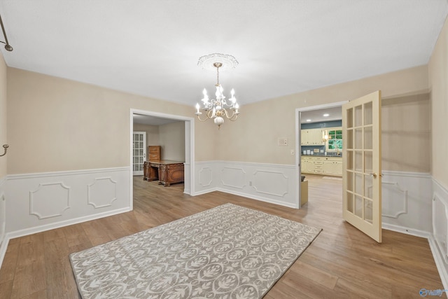 dining area with wood finished floors, a wainscoted wall, french doors, and an inviting chandelier