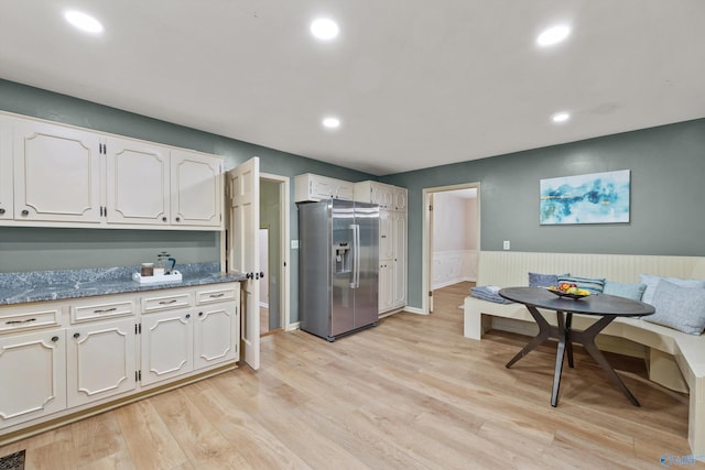 kitchen featuring stainless steel refrigerator with ice dispenser, breakfast area, white cabinets, light hardwood / wood-style flooring, and dark stone counters