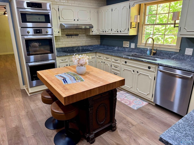 kitchen with wood finished floors, a sink, wooden counters, stainless steel appliances, and under cabinet range hood