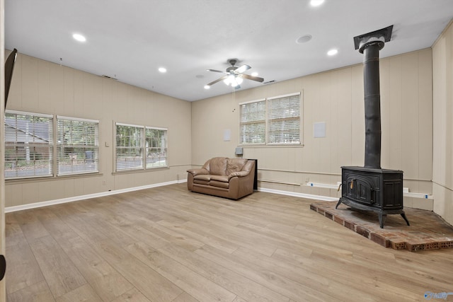 sitting room with ceiling fan, light hardwood / wood-style flooring, and a wood stove