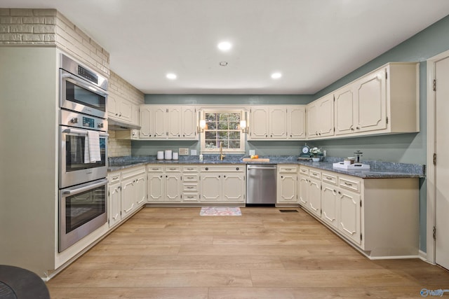 kitchen with recessed lighting, stainless steel appliances, dark countertops, a sink, and light wood-style flooring