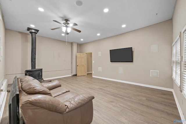 living room featuring ceiling fan, light hardwood / wood-style flooring, and a wood stove