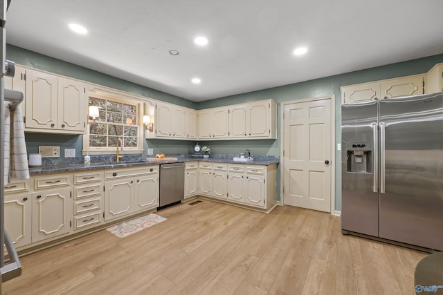 kitchen with light wood finished floors, a sink, dark countertops, recessed lighting, and appliances with stainless steel finishes