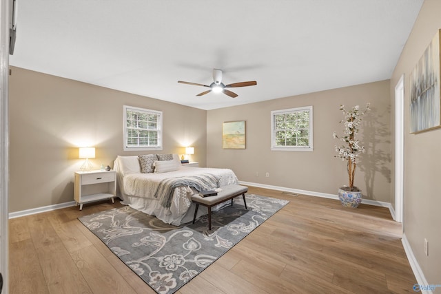 bedroom with ceiling fan, baseboards, multiple windows, and wood finished floors
