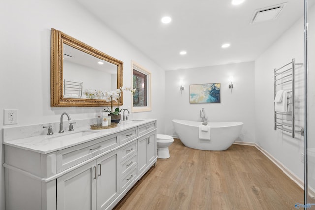 full bathroom featuring wood finished floors, a sink, double vanity, a freestanding bath, and visible vents