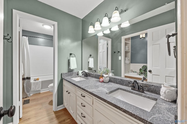 bathroom with toilet, wood finished floors, a sink, and double vanity